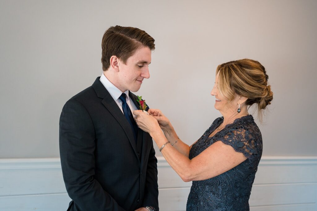 groom's mother pins white boutonniere on the lapel of his navy suit