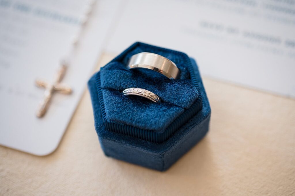 two wedding rings displayed in a blue velvet box next to a wedding invitation