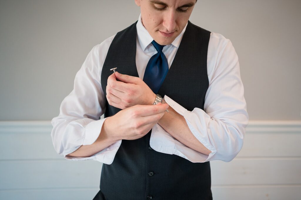 groom places watch on his wrist while dressing for his wedding