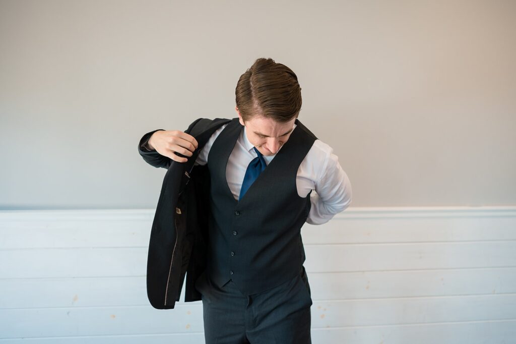 groom wearing a navy suit puts his jacket on 