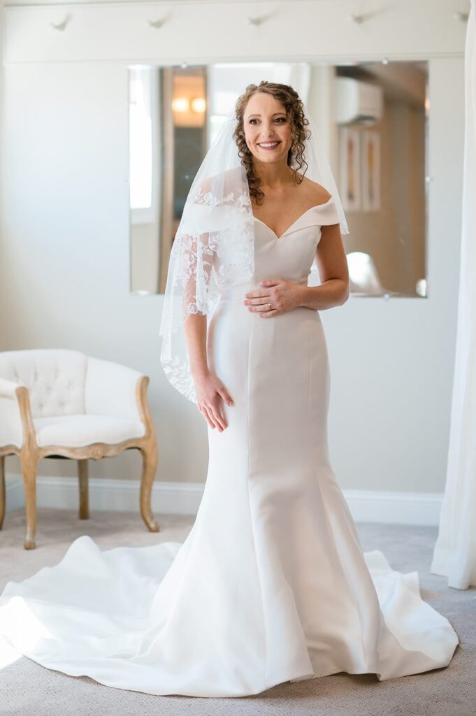 bride wearing white wedding dress with veil smiles in the bridal suite at the hounds in stonington ct