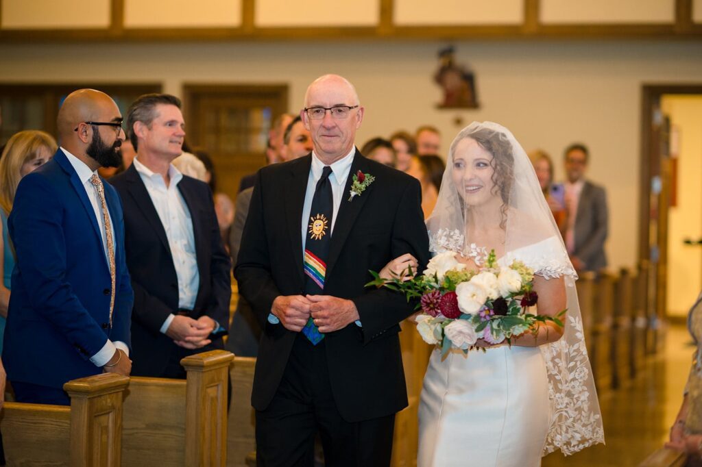 bride walks down the aisle wearing a white dress and veil on the arm of her father