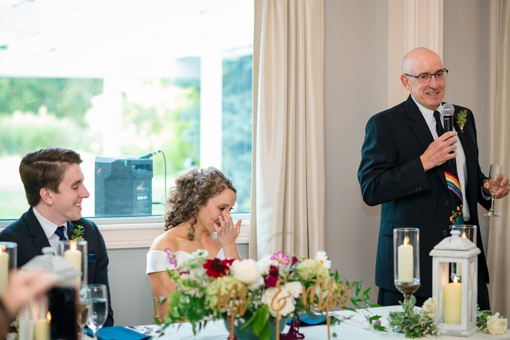 bride smiles and claps during her father's toast at her wedding