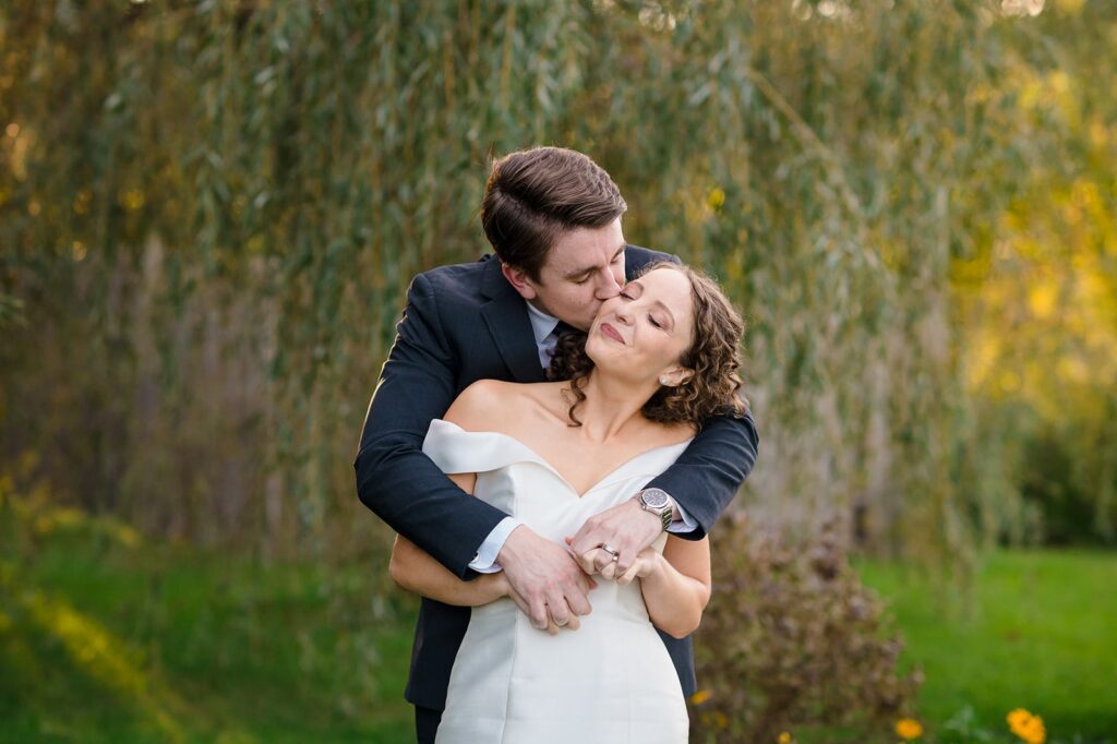 groom kisses bride with his arms wrapped around her shoulders