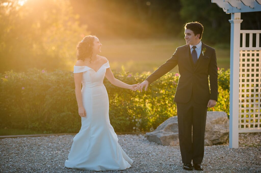 bride and groom walk together holding hands in the sunset at their stonington ct wedding