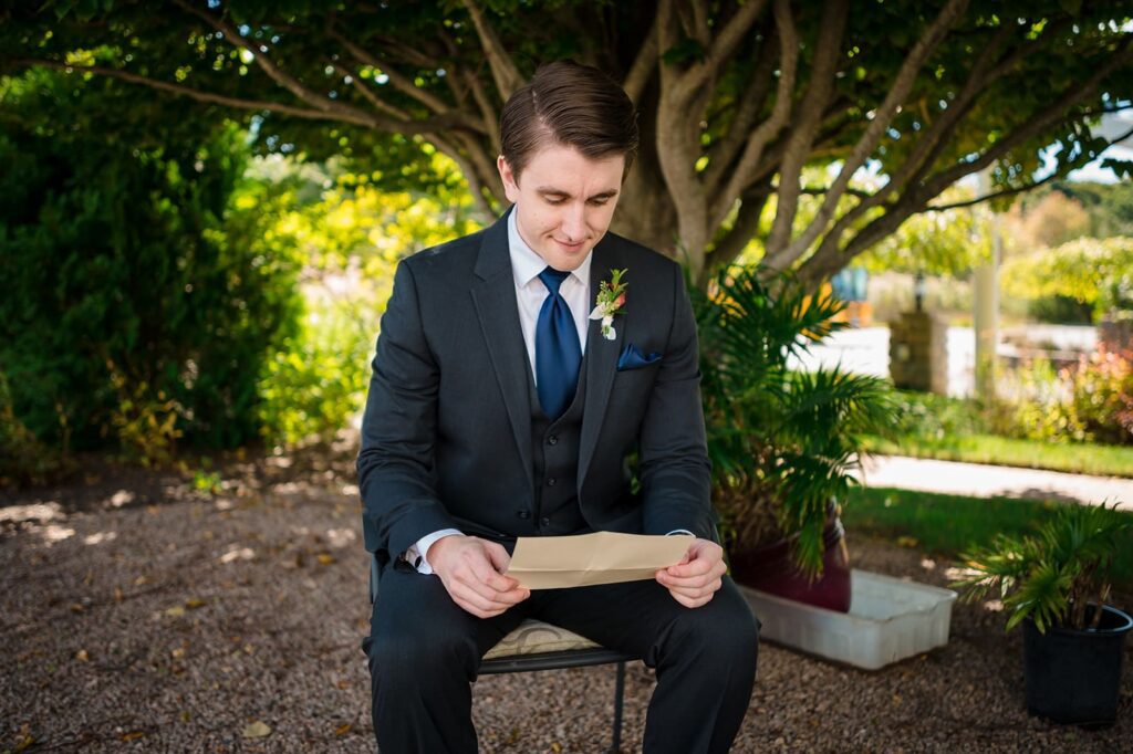 Groom sits under a tree reading a letter from his bride