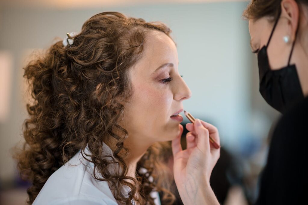 makeup artist applies lipstick to bride's face 