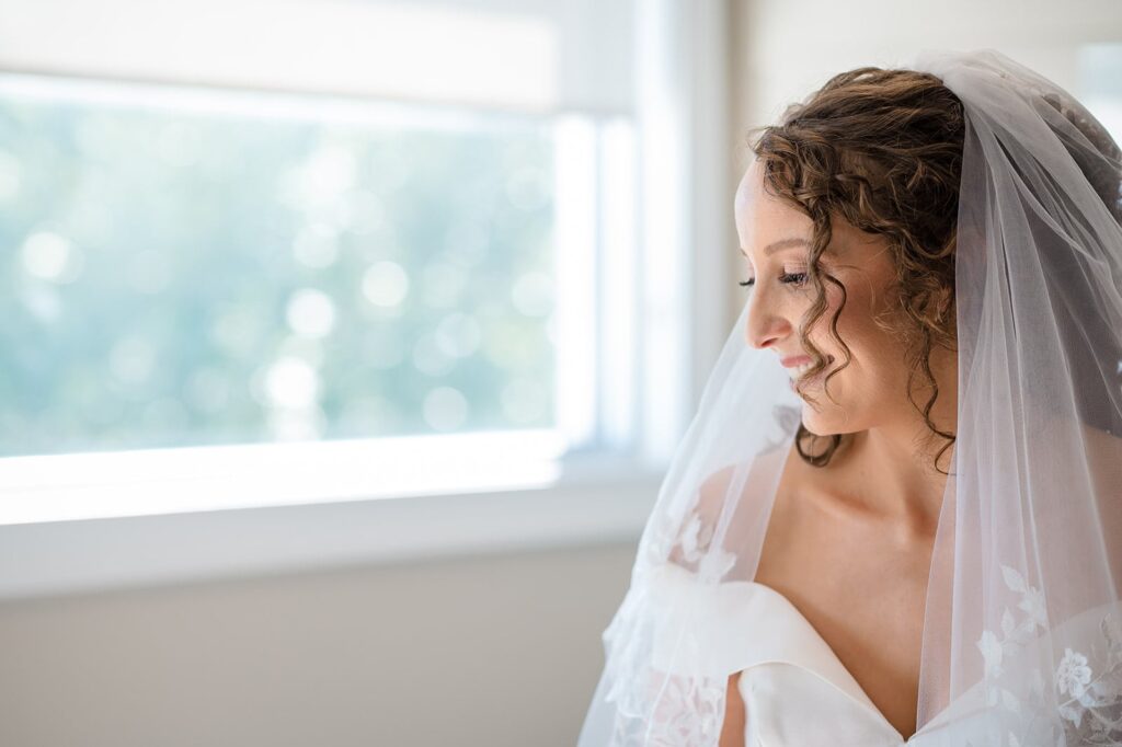 bride smiles over her shoulder near a window in the bridal suite at the hounds in stonington ct