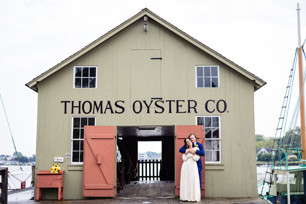 The historic Thomas Oyster Co. building serves as a unique backdrop for a wedding, with the couple embracing in front, adding a touch of maritime charm to their special day
