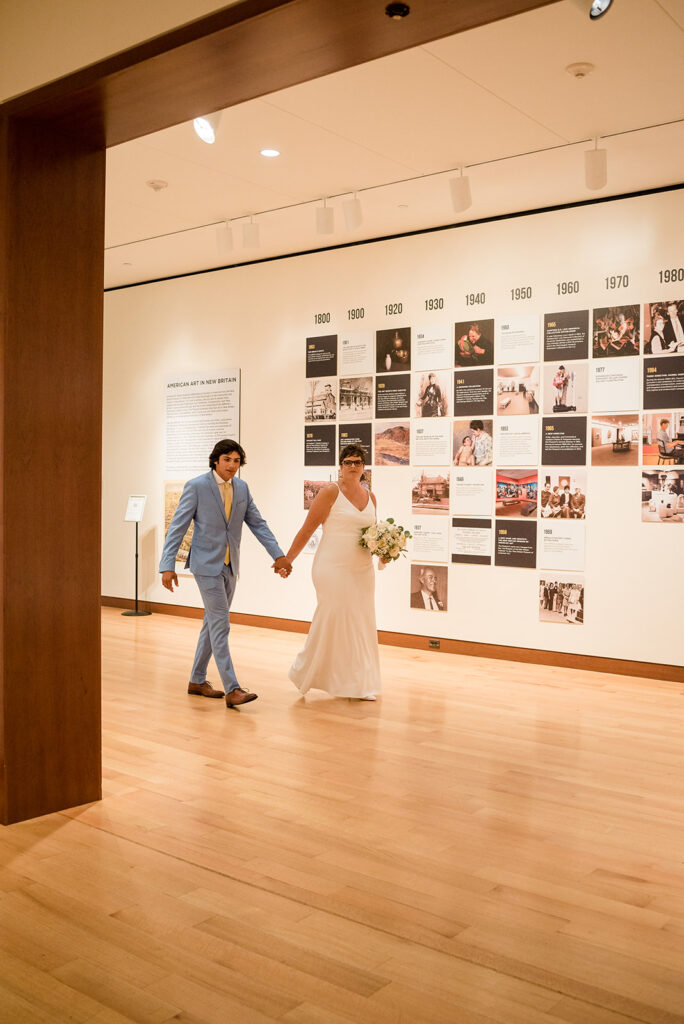 A newlywed couple walks hand in hand through an art gallery, their path lined with a historical timeline, merging their new beginning with the legacy of art history.