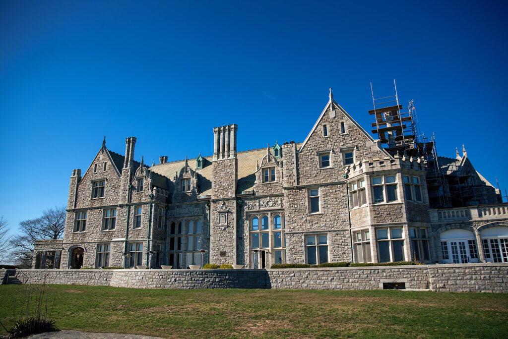 A historical stone mansion with scaffolding on one side under a clear blue sky, representing ongoing restoration efforts.