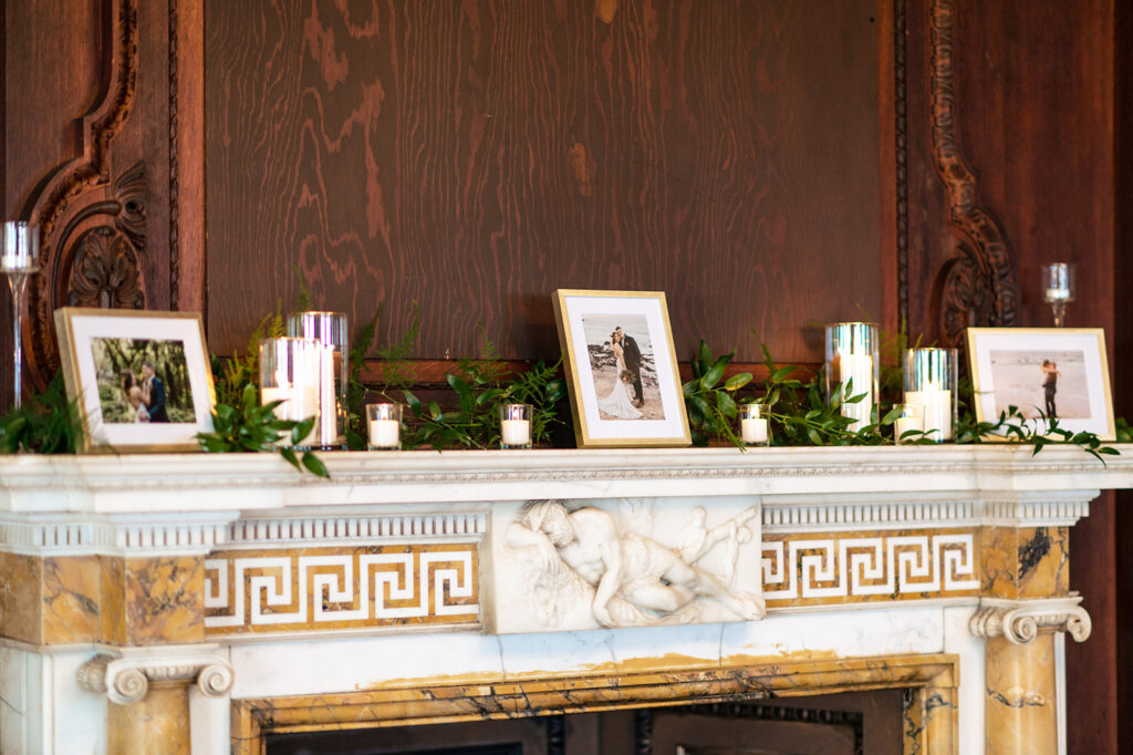 An elegant fireplace mantel adorned with framed photos, candles, and lush greenery, creating a cozy and personalized wedding atmosphere