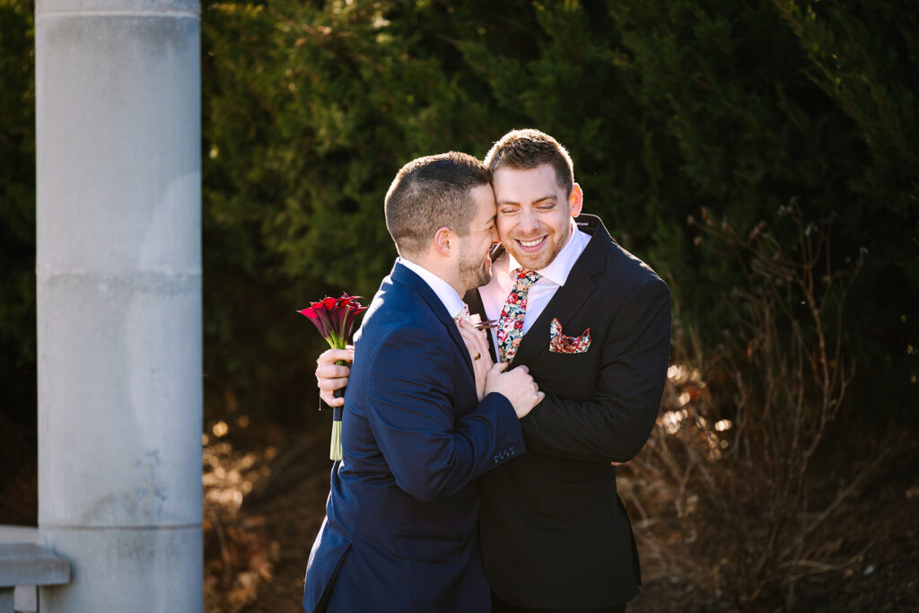 Two men in suits hugging and holding flowers.