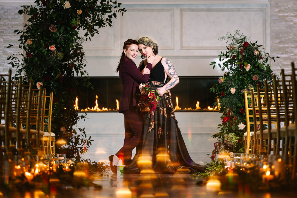 Two women in formal attire hugging in front of a fireplace at Grand View Mendon MA. 