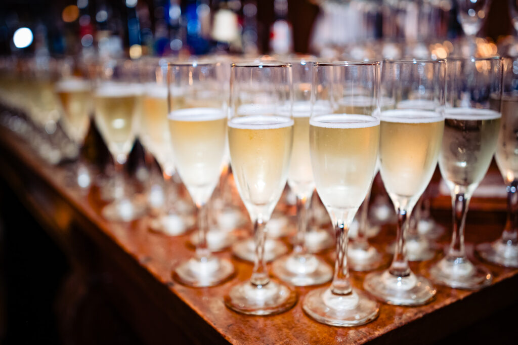 Rows of champagne flutes on a rustic wooden counter, effervescing with bubbly champagne, waiting to be served at a wedding reception.