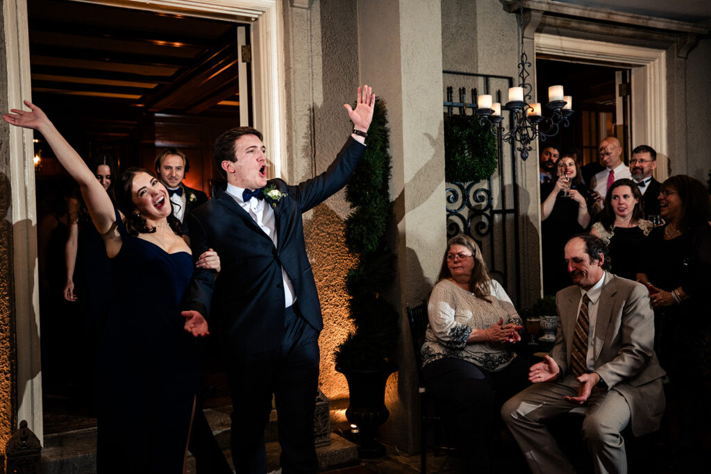 A jubilant bride and groom making a grand entrance, with arms raised in celebration, greeted by applauding guests