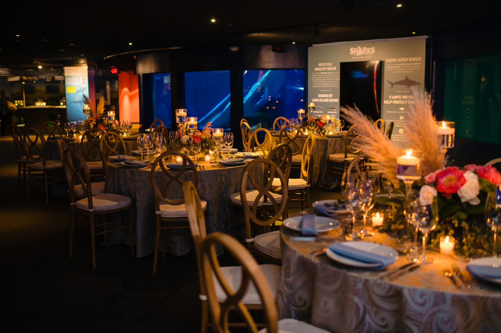 A sophisticated wedding reception space at an aquarium with elegantly set tables, ambient lighting, and a panoramic view of marine life