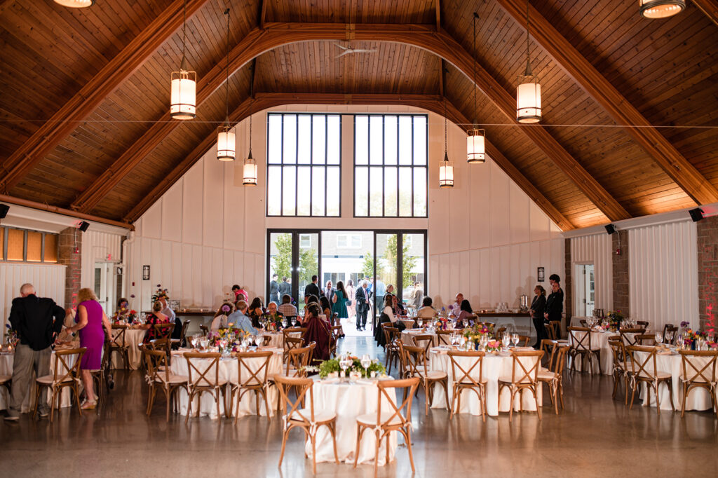 Interior view of a wedding venue with high wooden ceilings, pendant lights, and tables set for guests, ready for a celebration.