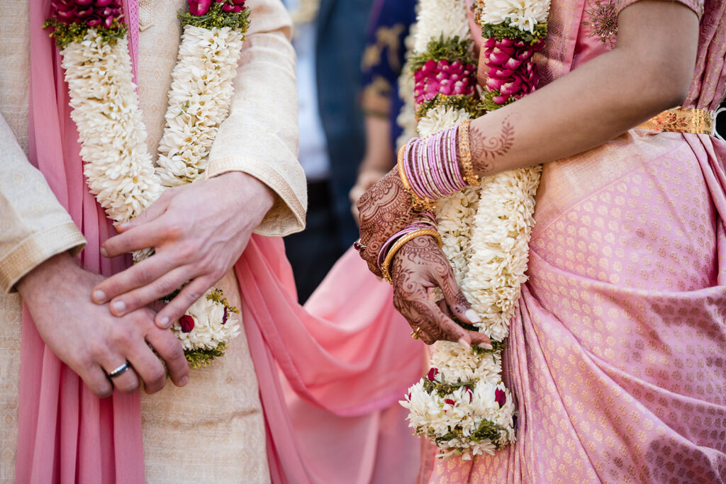 Close-up of the bride and groom's hands during a traditional Indian wedding ceremony; the bride's hands are decorated with intricate henna designs.