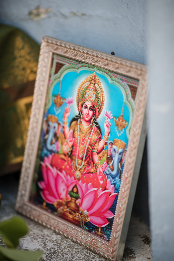 Close-up of a vibrant Hindu deity illustration, framed and placed on a shrine, surrounded by ceremonial items and flowers.