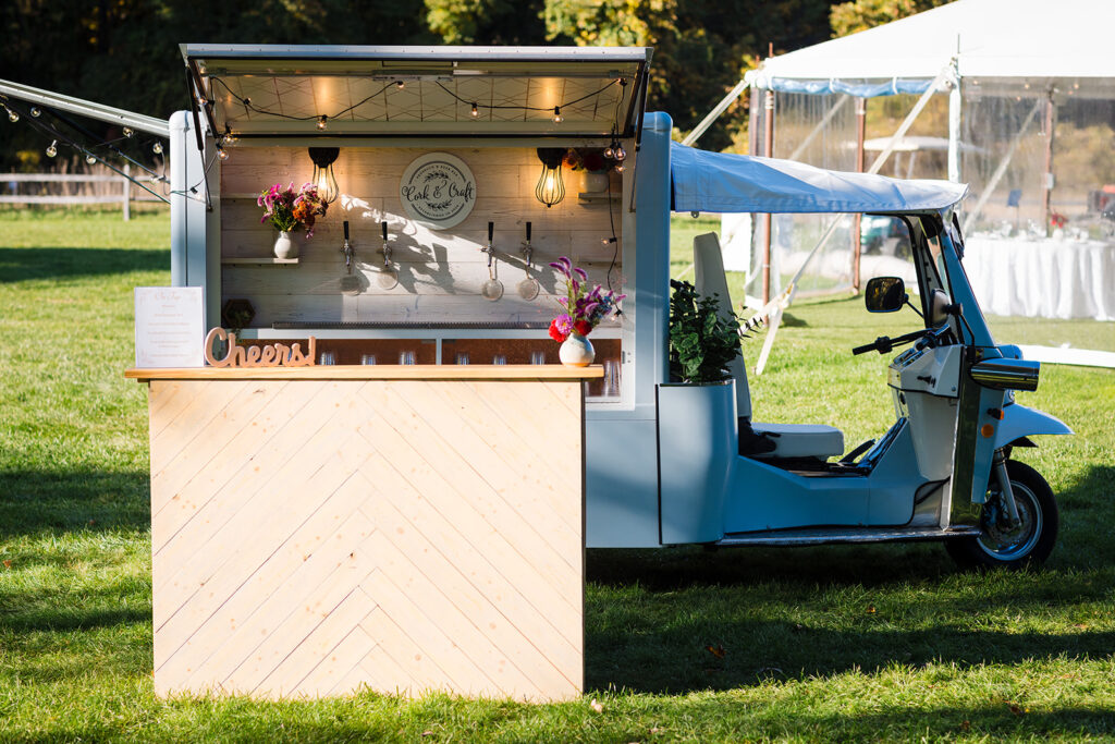 A charming mobile bar setup in a small blue and white vehicle with a wooden counter, offering refreshments outdoors.