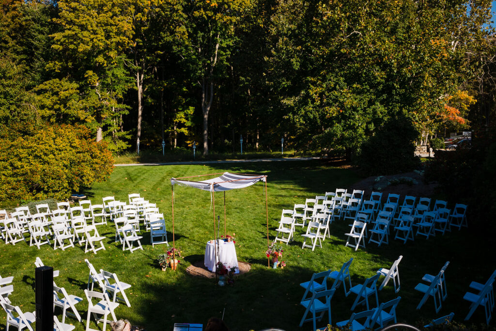 An aerial view of an outdoor wedding ceremony setup with white chairs arranged on a lawn and a chuppah waiting for the couple.