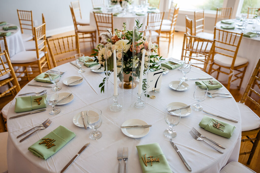 A wedding reception table elegantly set with white linens, green napkins, gold chairs, and a floral centerpiece, ready for a festive celebration.