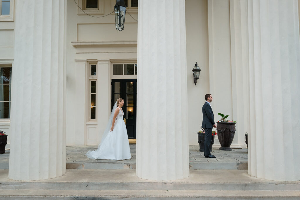 Bride and groom standing apart between white columns at the entrance of Wadsworth Mansion, looking towards each other with anticipation